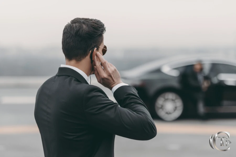 Chauffeur en costume debout à côté d’une Mercedes de luxe, concentré sur la sécurité.