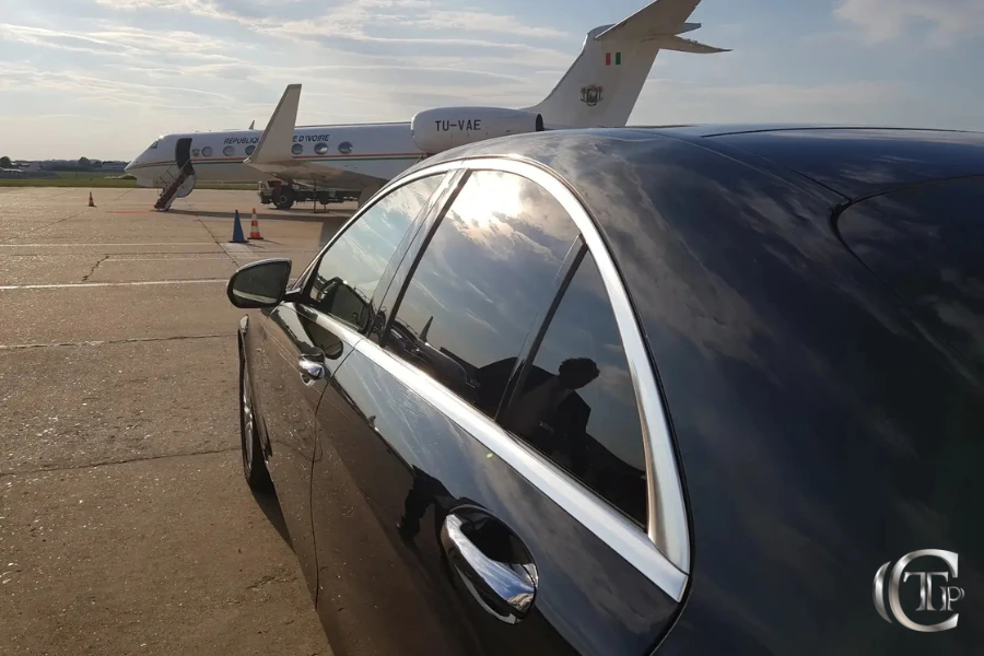 Luxury black Mercedes parked next to a private jet on airport tarmac under a blue sky.
